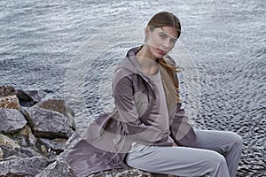 Beautiful sexy young blond woman with long hair and soft natural makeup wearing jacket designer suit sitting in rock stone beach