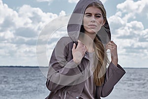 Beautiful sexy young blond woman with long hair and soft natural makeup wearing jacket designer suit sitting in rock stone beach