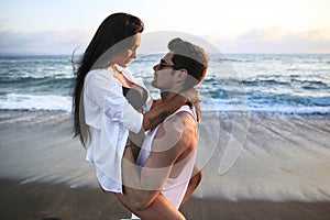 Beautiful, sexy, young caucasian couple cuddling on the beach at sunset time near ocean during summer vacation o