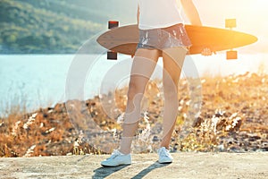 Beautiful sexy young girl in short shorts stands with longboard in sunny weather.