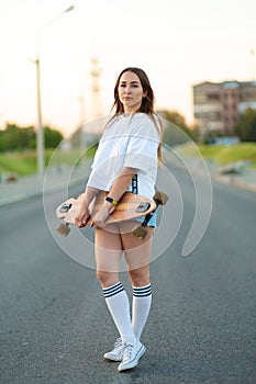 Beautiful sexy young girl in short shorts walking with longboard in sunny weather. Leisure. Healthy lifestyle. Extreme sports.