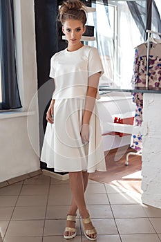 Beautiful young woman in beautiful fashionable white dress in the studio posing for the camera fashion shoot for the clothing