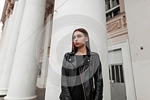 Beautiful sexy young woman in fashionable black clothes posing in the city near a white building with vintage columns. Attractive