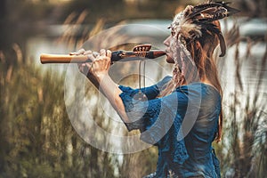 Beautiful shamanic girl playing on shaman flute in the nature.