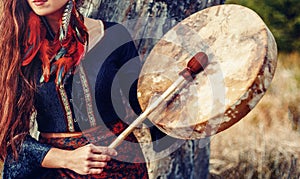 Beautiful shamanic girl playing on shaman frame drum in the nature.