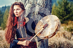 Beautiful shamanic girl playing on shaman frame drum in the nature.