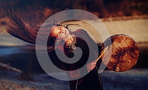 Beautiful shamanic girl playing on shaman frame drum in the nature.