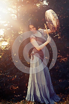 Beautiful shamanic girl playing on shaman frame drum in the nature