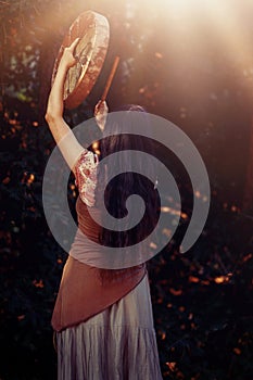 Beautiful shamanic girl playing on shaman frame drum in the nature