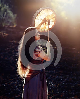 Beautiful shamanic girl playing on shaman frame drum in the nature