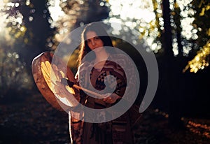 Beautiful shamanic girl playing on shaman frame drum in the nature