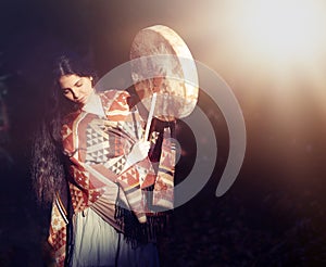 Beautiful shamanic girl playing on shaman frame drum in the nature