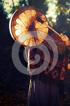Beautiful shamanic girl playing on shaman frame drum in the nature