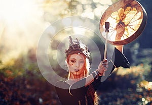 Beautiful shamanic girl playing on shaman frame drum in the nature