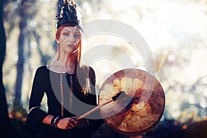 Beautiful shamanic girl playing on shaman frame drum in the nature