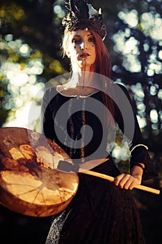 Beautiful shamanic girl playing on shaman frame drum in the nature