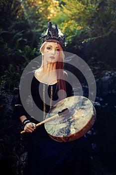 Beautiful shamanic girl playing on shaman frame drum in the nature