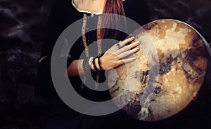 Beautiful shamanic girl playing on shaman frame drum in the nature.