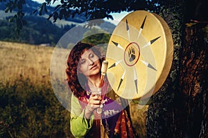 Beautiful shamanic girl playing on shaman frame drum in the nature.