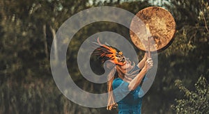 Beautiful shamanic girl playing on shaman frame drum in the nature.