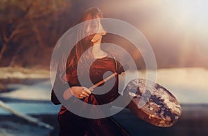 Beautiful shamanic girl playing on shaman frame drum in the nature and light graphic effect.