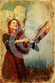 Beautiful shamanic girl playing on shaman frame drum in the nature, old efect.