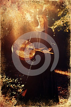Beautiful shamanic girl playing on shaman frame drum in the nature, old photo effect