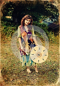 Beautiful shamanic girl playing on shaman frame drum in the nature, old photo effect.