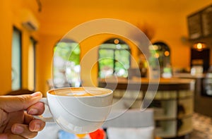 Beautiful shape foam cappuccino coffee cup in man hand holding up in yellow classic background with copy space