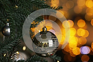 Beautiful shiny holiday bauble hanging on Christmas tree against blurred fairy lights, closeup. Space for text