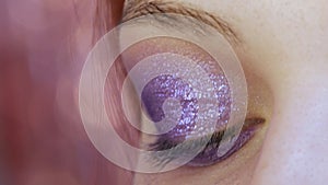 Beautiful shiny violet-lilac shadows are applied with a special brush on the eyelid of the model. The process of bright