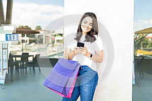 Beautiful Shopper Smiling While Using Smartphone In Shopping Center