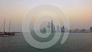 Beautiful shot of Abu Dhabi city skyline towers and beach at sunset - Big wooden boat at the beach