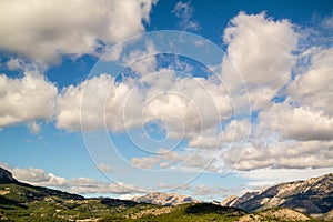 Beautiful shot of a blue sky full of clouds above mountains covered in trees in Polop, Spain