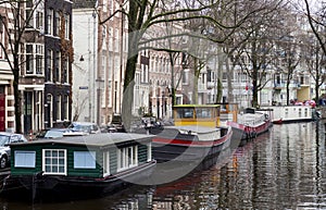 Beautiful shot of the boats docked on the riverside in Amsterdam with trees and architectures