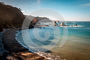 Beautiful shot of a calm sea with hills on the side under a blue sky in Asturies, Spain photo