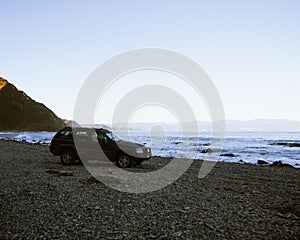 Beautiful shot of a car parked on a beach against ocean waves