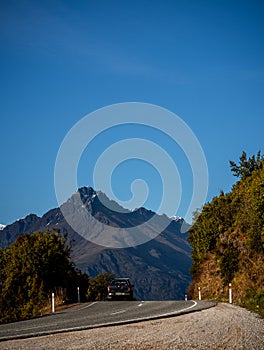 Beautiful shot of a car on the road to Glenorchy with a mountain in the background taken at sunrise on a winter day in Queenstown