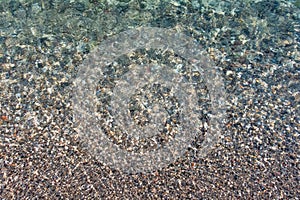 Beautiful shot of clear seawater and colorful pebbles underneath reflecting sunlight