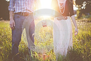 Beautiful shot of a couple holding hands while standing in a grassy field with sun in background