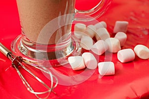 Beautiful shot of a glass of chocolate milkshake and marshmallows on a red table