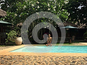 Beautiful shot of a male sitting near the pool with surrounded by trees at daytime