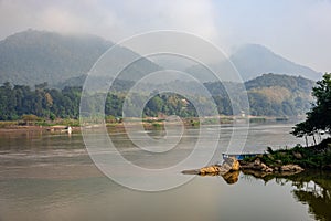 Beautiful shot of the Mekong River with a floating boat near mountains in Luang Prabang, Laos