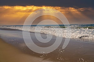 A beautiful shot of miles of vast blue ocean water and waves rolling into a beach with silky brown sand with powerful clouds