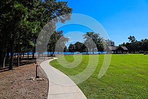A beautiful shot of a park on the lake with vast green grass, blue lake water, lush green trees and blue sky