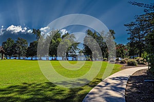 A beautiful shot of a park on the lake with vast green grass, blue lake water, lush green trees and blue sky