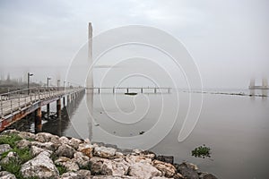 Beautiful shot of a rocky coast by the Vasco of Gama bridge in  foggy weather in Lisbon, Portugal