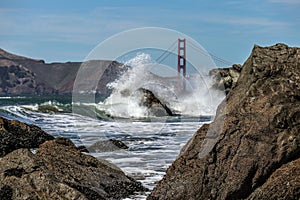 Beautiful shot of sea waves crashing on massive rocks with a background of the Golden Gate Bridge
