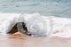 Beautiful shot of splashing sea waves covering the rock on a sunny day