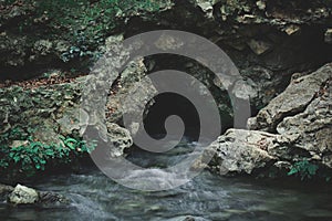 Beautiful shot of a streaming river coming out of cave in middle of rocks.